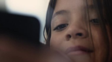 Çevrimiçi medyada akıllı telefon cihazına bakan küçük kızın yakın yüzü ve gözleri. Çocuk eğlence içeriğiyle hipnotize edildi