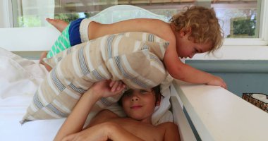 Kardeşler evde yastıkla oynuyorlar, yeni yürümeye başlayan çocuk ağabeyinin üstünde.