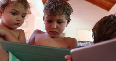 Çocuklar evdeki tablet ekrana bakıyor, oturma odasındaki kanepede oturuyor.