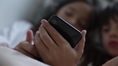 Çevrimiçi medya eğlencesi tarafından emilmiş, arka planda bulanık çocuklar telefon ekranına bakıyor.