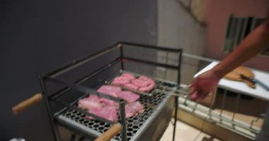 Afrika kökenli Amerikalı bir adam çatıdaki barbeküde et pişiriyor, biftek ve sosisleri kontrol ediyor ve canlı bir şehir ortamında yemek hazırlıyor.