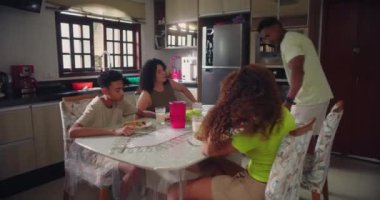 Aile öğle yemeğinden önce dua etmek için el ele tutuşur. Sıcak bir mutfak ortamında yemek masasında bir bağ ve birlik anı yaratır.