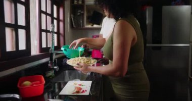 Anne mutfak lavabosundaki makarnayı kuruturken aile yemek hazırlama, takım çalışması ve aile mutfağında kaynaşma konularında yardımcı oluyor.