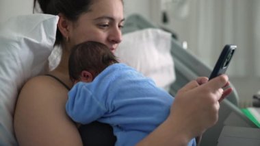 Yeni anne hastane yatağında yeni doğmuş bebekle akıllı telefon kullanıyor, ebeveynliği ve teknolojiyi dengeliyor, sağlık hizmetleri, doğum sonrası bakım, aile bağları, modern annelik sorunları