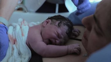 Doğumdan hemen sonra yeni doğmuş bir bebeğin ilk saniyeleri annesinin göğsünde dinlenmek için çırpınıyor deriyle teması vurguluyor, bir insanın ilk ağlayışları...