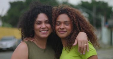 Anne ve kızı dışarıda kollarını açmış, gülümsüyor ve güçlü ilişkilerini, sıcaklıklarını ve beraberliklerini barışçıl bir mahallede kutluyorlar.