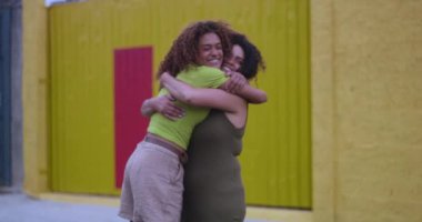 Afrika kökenli anne ve kızı neşeli bir gülümsemeyle kucaklaşıyorlar, sıcak ve sevgi dolu bir kucaklaşmayı açık havada paylaşıyorlar.