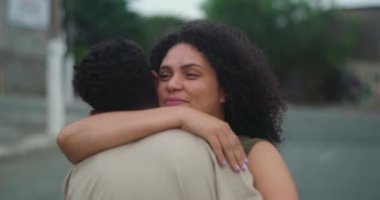 Anne, genç oğluna sımsıkı sarılıyor sıcak bir gülümsemeyle, açık havada sevgi ve sevgi dolu bir anın tadını çıkarıyor.