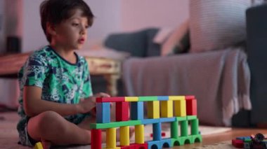 Çocuk bağdaş kurarak yerde oturuyor, pembe kalemle resim çizerken, konsantrasyonunu, yaratıcılığını ve sanatsal veya öğrenme aktivitelerine olan bağlılığını ifade ediyor.