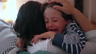 Anne ağlayan çocuğu duygusal kucaklamayla teselli eder, eller nazikçe tutar, sevgiyi, korumayı ve bakımı ifade eder, sıkıntı anında aile desteği, yakın çekim anı