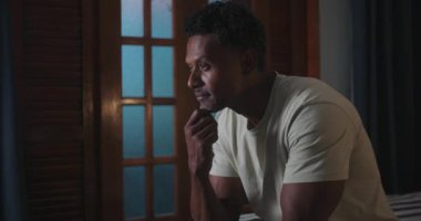 Siyah bir adam yakın planda, derin derin düşüncelere dalmış, derin düşüncelere dalmış, derin düşüncelere dalmış, ahşap arka planda sıcak bir iç mekan ortamında.