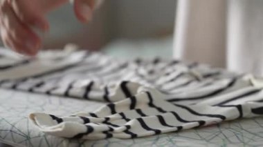 Ütü, hassasiyet ve bakım sırasında çizgili kumaşı tutan eller, kumaş hizasına dikkat, angarya sırasında el hareketlerinin yakın çekimi, ütü işinin ayrıntılı görünümü