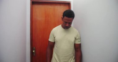 Afrika kökenli bir adam koridor duvarına yaslanmış, elleri alnında, iç gözlem yapıyor ve iç mekanda duygusal yorgunluk yaşıyor.