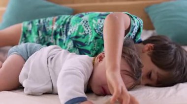 Bebek yatakta ağlarken, büyük kardeş yakınlarda uzanıyor, kardeş bağı ve doğal duygularla şefkatli ama gerçekçi bir aile anı sergiliyor.