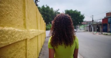 Güney Amerika şehir merkezinde sakin bir sokakta yürüyen Latin kökenli genç, doğal kıvırcık saçlı, yeşil ve renkli duvarlarla çevrili.