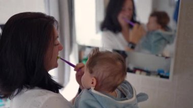 Anne kucağında bebek varken diş fırçalama, bebek aynasında izleme, sabah bakım rutini, aile bağları, günlük temizlik, annelik anları, ebeveyn-çocuk etkileşimi