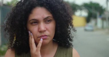 Kadın dışarıda duruyor, elleri yüzü üzerinde dinleniyor, derin derin derin düşünüyor, içe dönük an, duygusal yansıma, belirsizlik, kişisel mücadele ve sessiz esneklik.