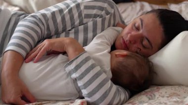 Anne kestirirken bebeğe sarılıyor, sıcaklığı besliyor, sessiz bir aile anı, huzurlu bir bağ kuruyor, huzur içinde dinleniyor.