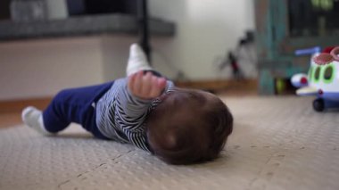 Bebek yerde yatıyor, kollar havada yuvarlanmaya çalışırken motor beceriler, güç ve koordinasyonla ilgili erken gelişim kilometre taşını gösteriyor.
