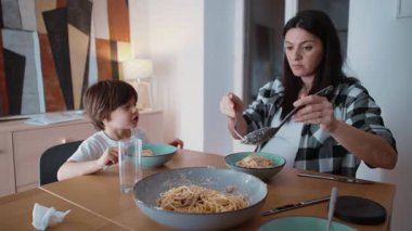 Anne ve çocuk gece evde yemek saatinde, anne ve babasının spagetti servis ederken oğluyla etkileşime girdiği samimi aile sahneleri.