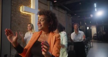 Kilisede ibadet sırasında alkışlayan ve gülümseyen çeşitli insanlar, arka planda parlayan haç, neşe, birlik ve ruhsal bağlantı ifadeleri