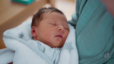 Kollarında dinlenen yeni doğmuş bir bebeğin nazikçe yakın plan çekimi bir bebeğin hayatının ilk günlerini vurguluyor.