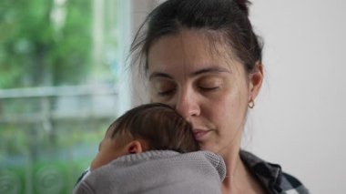 Anne gözleri kapalı, yeni doğmuş bebeğini kucağında tutuyor, huzurlu bir dinlenme anı yakalıyor ve samimi bir bağ kuruyor.