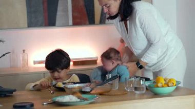 Anne kucağında bir bebek, küçük çocuk yemek masasında yemek yerken, çoklu ebeveynlik anlarında, aile içi ilişkilerde, ve günlük yemek saatlerinde bağ kurmada.