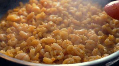 Tavada pişirilen karideslerin yakın çekimi buhar yükseliyor, portakal spatulası taze deniz ürünlerini karıştırıyor, sulu dokuya ve taze ev yapımı bir tabakta canlı renge vurgu yapıyor.