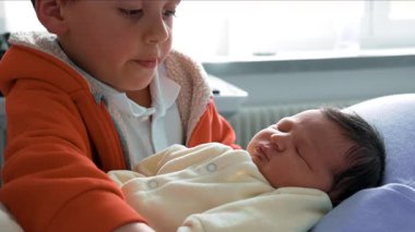 Büyük kardeş, yeni doğmuş bir bebeği harika ve özenli bir bakışla tutuyor. Yürek ısıtan bir sahnede kardeşler arasındaki bağı ve sevgiyi yakalamak.