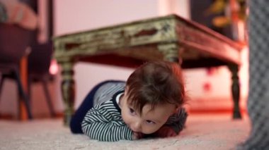 Bebek yerde yatıyor, elleri şaşırmış bir ifadeyle destekleniyor, kırsal ahşap masanın yanında mideye yakın vakit geçiriyor, çevreyi keşfediyor, erken gelişim motor aktiviteleri yapıyor.