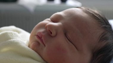 Yeni doğmuş bebek gözleri kapalı, yumuşak krem bir kıyafet içinde huzur içinde dinleniyor. Erken yaşlardaki sükunet ve masumiyeti vurgulayarak, bebeğin narin özelliklerini ve huzurlu ifadesini yakalar.