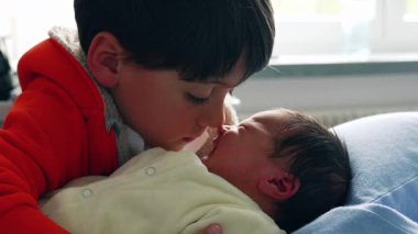 Genç bir çocuk ve yeni doğmuş bir bebek, burunları nazikçe birbirine değen, samimi bir anı paylaşıyorlar. Yakın temas, aile sahnesinde güçlü kardeş bağını ve saf sevgiyi vurgular.