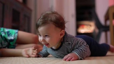 Bebek yerde yatıyor, kollarıyla yukarı itiyor, heyecanlı bir ifadeyle ağzı açık, neşeli bir an yaşıyor, erken motor becerilerini gösteriyor, kapalı alanda enerjik bir ortam.