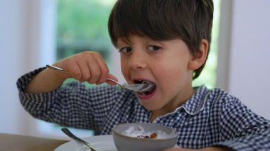 Genç bir çocuk masada bir kase mısır gevreği yiyor, sıcak bir evde yemeğinin zevkine odaklanıyor.