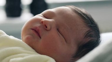 Yeni doğmuş bebek huzurlu bir ifadeyle uyuyor, yumuşak bir battaniyeye sarılmış. Yeni doğmuş bir bebeğin saflığını ve sükunetini vurgulayarak hassas özelliklerini ve huzurlu atmosferini yakalar.