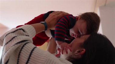 Anne havadayken bebeği öpüyor. Sevgi ve kahkaha dolu neşeli bir an. Ev ortamında samimi bir aile ortamı.
