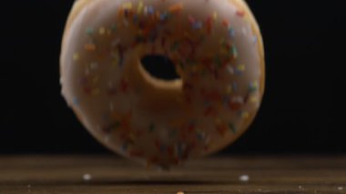 Büyük bir donut yavaş çekimde makro mercekle yakalanan masanın üstüne düşer ve şeker şekeri yuvarlanır.