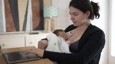 Odaklanmış bir anne dizüstü bilgisayarı üzerinde çalışırken bebeği kollarında huzurlu bir şekilde uyuyor, kariyer kavşağını vurguluyor ve günümüzün iş yerinde ebeveynlik yapıyor.
