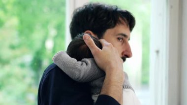 Bebeğin hayatının ilk haftasında yeni doğmuş oğlunu kucağında tutarken baba kameraya doğru dönüyor. Baba sıcakkanlılıkla gülümsüyor, şefkatli ve neşeli bir çocukluk anını yakalıyor.