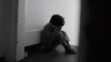 Evde Kötü Edebiyat Koridoru 'nda oturan, Ellerle Yüzü Kaplayan, Çocukluk Depresyonu ve Utanç Mücadelesini Açıklayan Tek Renkli Çocuk Görüntüsü