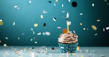 Cupcake 'in üzerine konfeti düştü, üstünde bir mum vardı, deniz mavisi arka planında çok yavaş çekimde çekilmişti. Doğum günü konsepti kutlaması