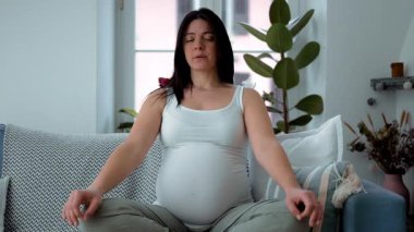 Üçüncü üç aylık dönemde hamile kadın kanepe üzerinde meditasyon yapıyor. 30 'lu yaşlarda ev ortamında dinlenen kadın.