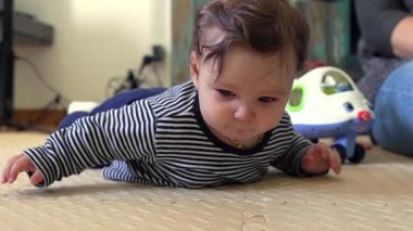 Bebek yerde yatıyor, ön kollara dayanıyor, ağzından tükürük kusuyor, sindirim ve erken gelişim aşamalarıyla ilgili doğal bebek davranışı.