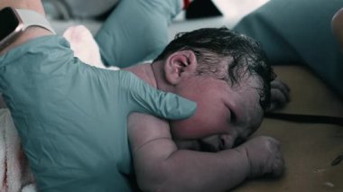 Çocuk doktoru, doğumdan sonra anne göğsü üzerine yeni doğan bebekleri inceliyor, erken sağlık hizmetlerini ve cilt temasını vurguluyor.