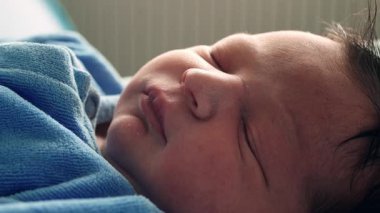 Yeni doğmuş bir bebeğin, yumuşak bir battaniyede, mavi bir tulumun içinde huzurlu bir şekilde uyuması, yeni doğmuş bir bebeğin sakin ve rahat bir ortamda uykusunun narin doğasını vurguluyor.