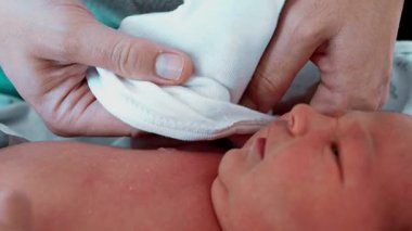 Annenin yeni doğan bebeği ilk günlerinde giydirmesi, bebeğin küçük ellerini ve kollarını nazikçe giydirmesi.