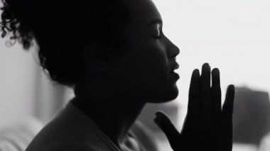 Bir dindar genç siyahi kadın dua ediyor, 20 'li yaşlarda, Afrika kökenli, gözleri kapalı bir kadın silueti monokromatik olarak Umutla ve İnançla