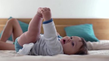 Bebek, rahat ve sıcak bir aile ortamında, erken çocukluğun neşeli ve neşeli anlarını yakalar ve ayaklarıyla yatakta uzanır.