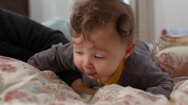 Bebek yatakta yatarken garip bir ifadeyle uzanıyor, annesinin koluyla destekleniyor, çevreyi keşfediyor, hassas aile bağları, sıcak ev ortamları, erken gelişim
